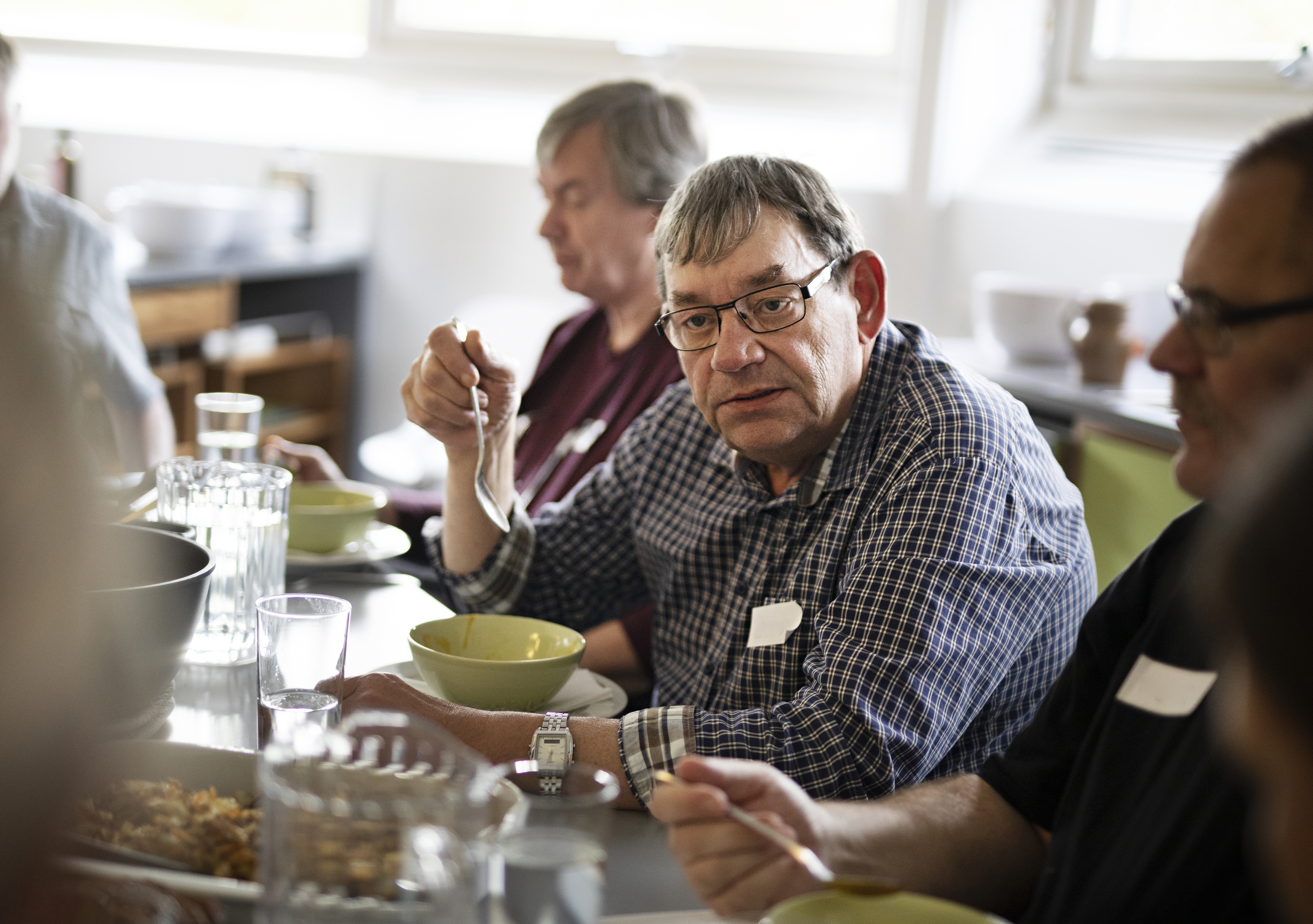 Et billede af en mand, der sidder ved et bord og spiser sammen med andre mennesker.