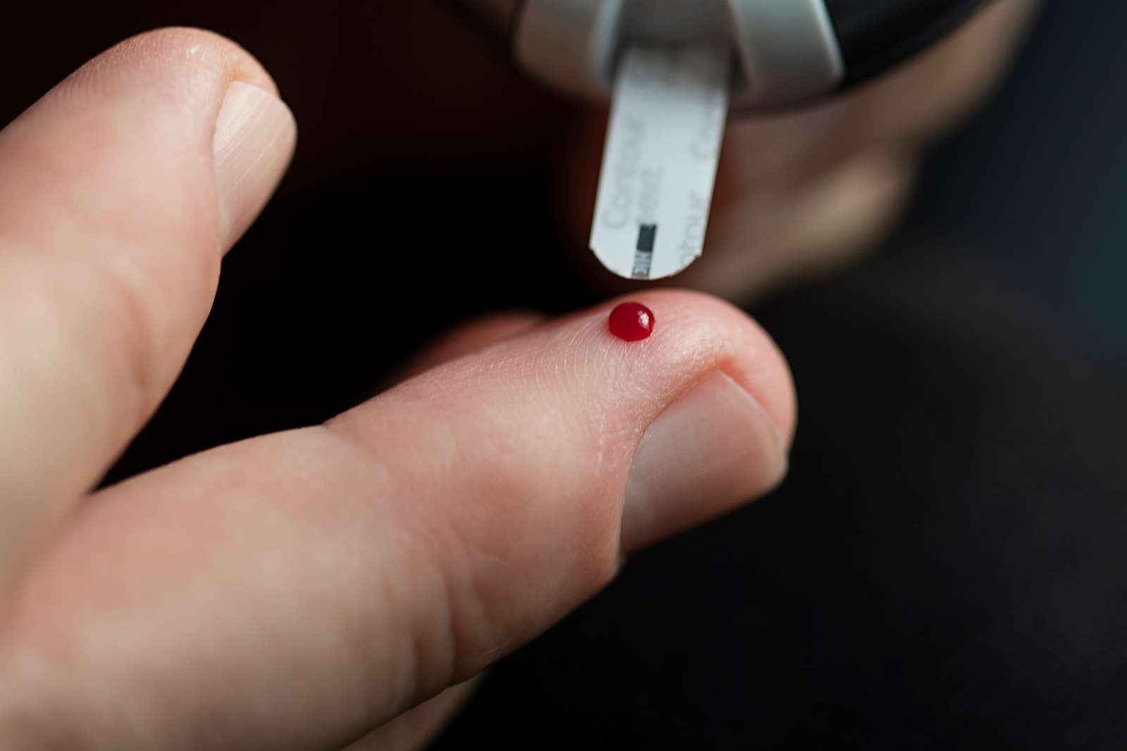 Billede af en bloddråbe på en finger, der bliver målt blodsukker fra.